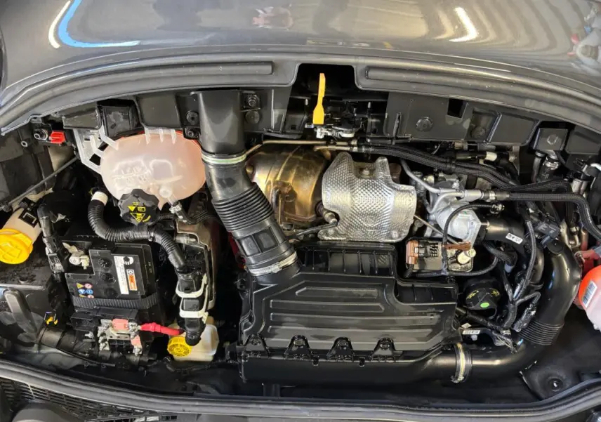 Vue plongeante sur le moteur gris d'une FIAT 500X MY23 1.5 FireFly hybride avec composants et durites visibles.