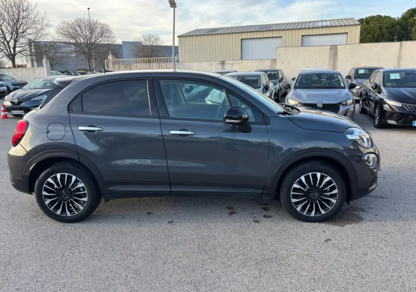 Profil droit d'un FIAT 500X gris 2023 avec jantes noires et argent classiques, stationné en extérieur.