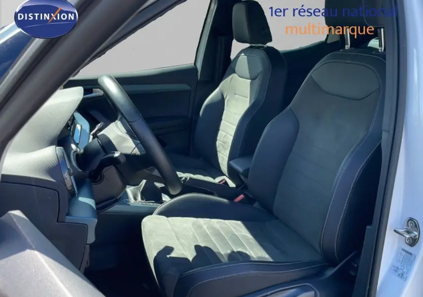 Vue intérieure côté conducteur du SEAT Arona 2025, sièges en tissu noir avec surpiqûres blanches, volant cuir multifonction.
