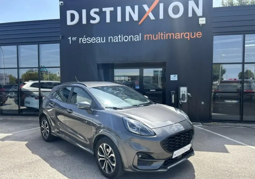 Ford Puma gris Magnetic en 3/4 avant droit avec jantes alliage et calandre noire ST-Line devant un bâtiment Distinxion.