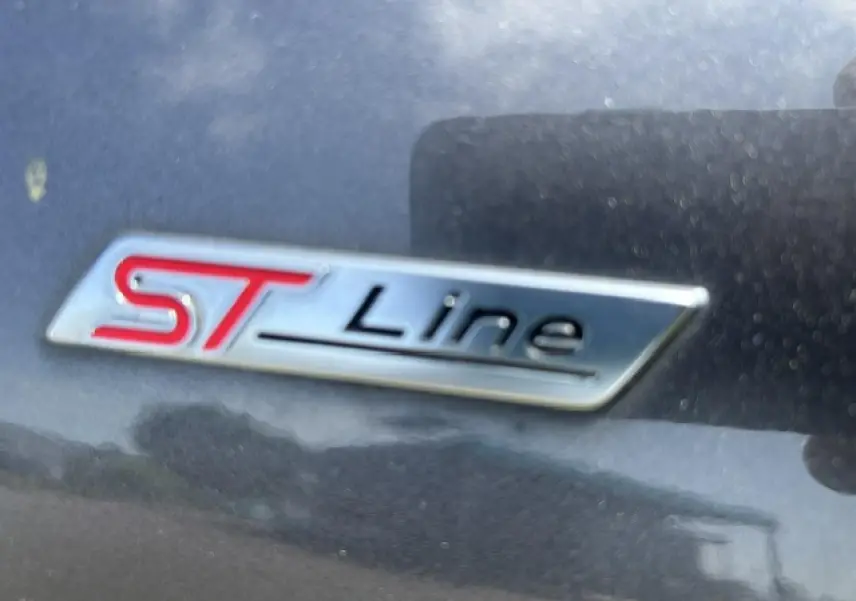 Gros plan sur le badge ST-Line rouge et noir sur la carrosserie gris magnetic d'une Ford Puma 2022.