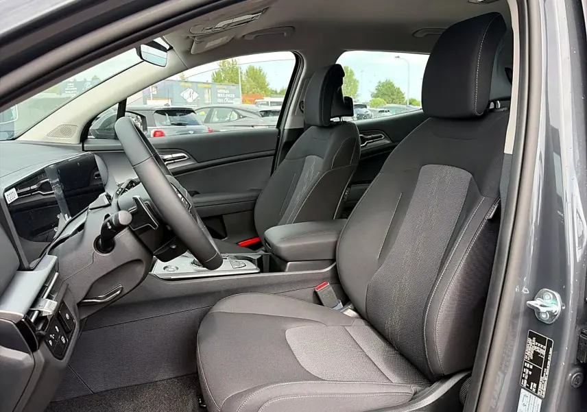 Vue intérieure côté conducteur du Kia Sportage 1.6 hybride gris eclipse, montrant sièges et volant multifonction cuir.