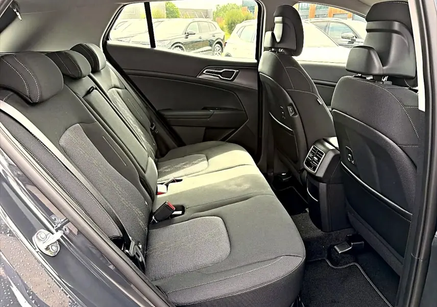Vue intérieure côté gauche des sièges arrière gris foncé du Kia Sportage 1.6 hybride 239 active avec accoudoirs et aérateurs centraux.