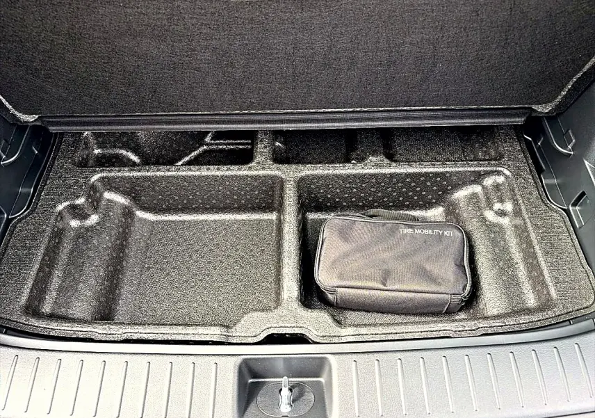 Coffre ouvert du Kia Sportage 1.6 hybride gris eclipse, vue sur le rangement sous plancher avec kit de mobilité pneus.
