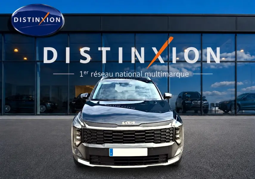 Vue frontale d'un KIA SPORTAGE 1.6 hybride 239 gris eclipse garé devant une vitrine avec logo Distinxion.