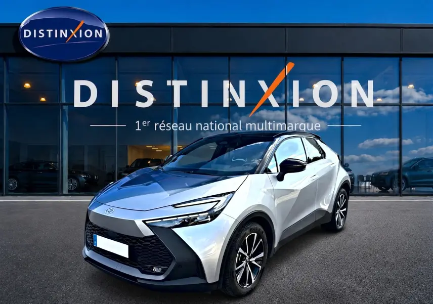 Toyota C-HR 1.8 hybride gris en 3/4 avant droit, avec toit noir et jantes alliage visibles devant un showroom Distinxion.