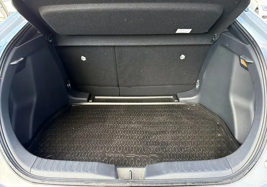 Coffre ouvert vu de face d’un Toyota C-HR gris, avec tapis de coffre noir texturé et banquette arrière rabattable.