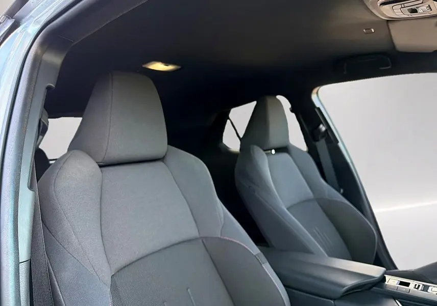 Vue intérieure des sièges avant en tissu gris foncé du Toyota C-HR 1.8 hybride 2025 avec accoudoir central.