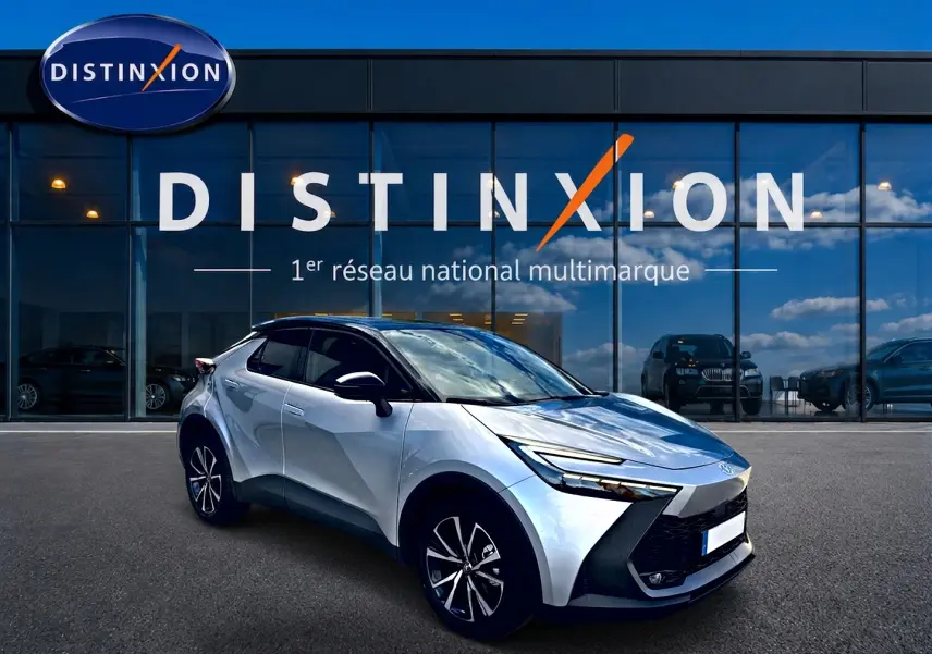 Toyota C-HR 1.8 hybride gris en 3/4 avant droit, avec jantes alu et calandre distinctive noire devant showroom Distinxion.