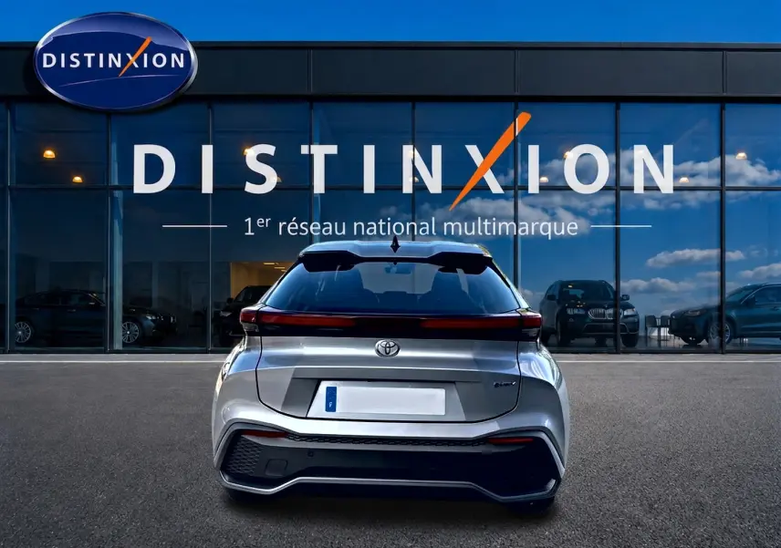 Vue arrière d'un Toyota C-HR gris 2025 hybride, avec feux arrière LED et logo Toyota visible devant une vitrine Distinxion.