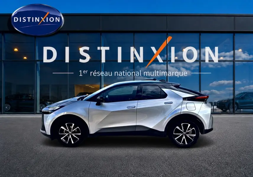 Toyota C-HR 1.8 hybride gris en profil droit devant une vitrine avec logo Distinxion en arrière-plan.