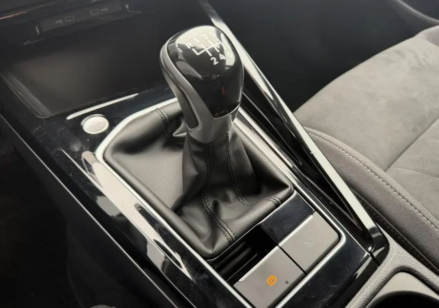 Gros plan sur le levier de vitesse manuel noir et cuir de la Volkswagen Golf VIII 1.5 TSI, avec console brillante autour.