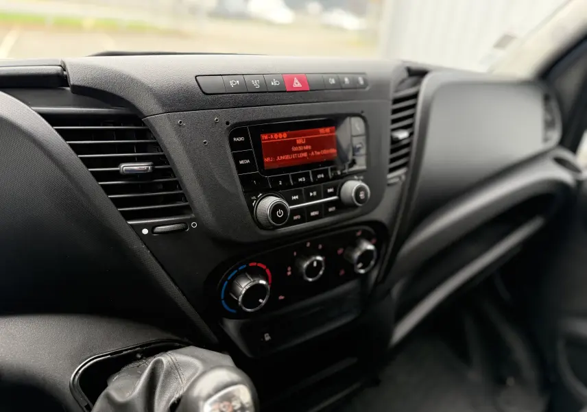 Vue rapprochée de la console centrale noire de l'Iveco Daily Fourgon 2017 avec radio et commandes de climatisation.
