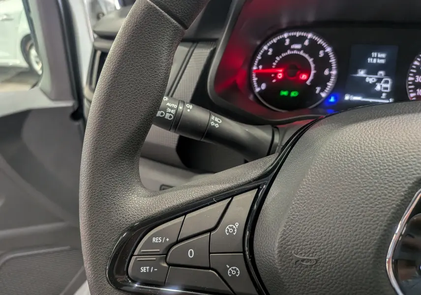 Gros plan sur le volant du Renault Trafic cabine approfondie 2023, montrant les commandes de régulateur de vitesse et le tableau de bord allumé.