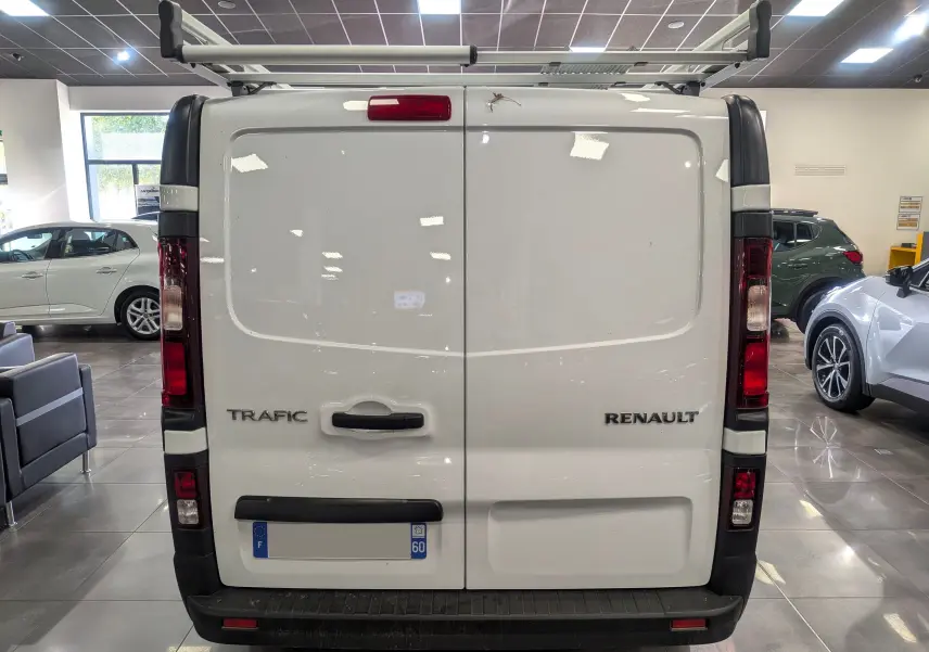 Vue arrière d'un Renault Trafic blanc minéral avec porte double et galerie de toit en intérieur showroom.