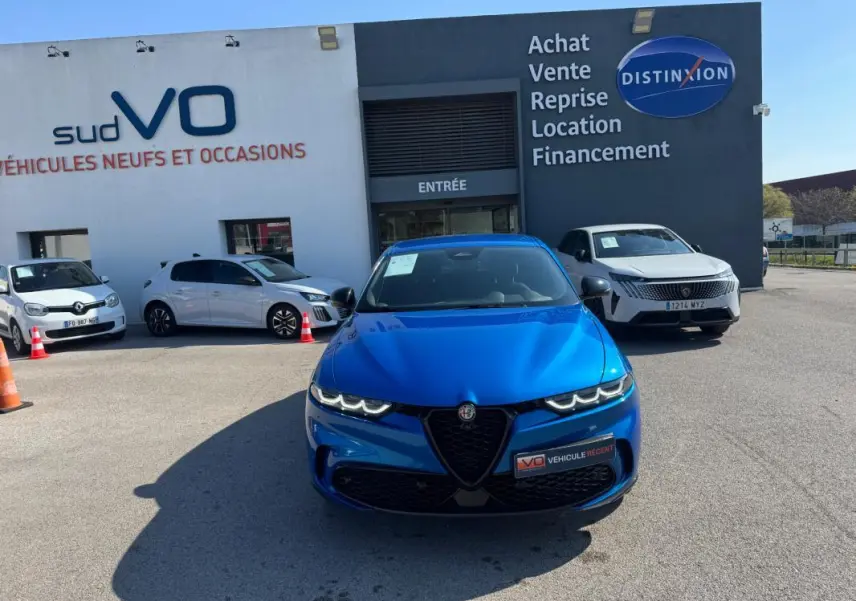 Vue avant d'une Alfa Romeo Tonale 1.5 Hybrid bleu foncé avec phares LED allumés sur un parking de concession.