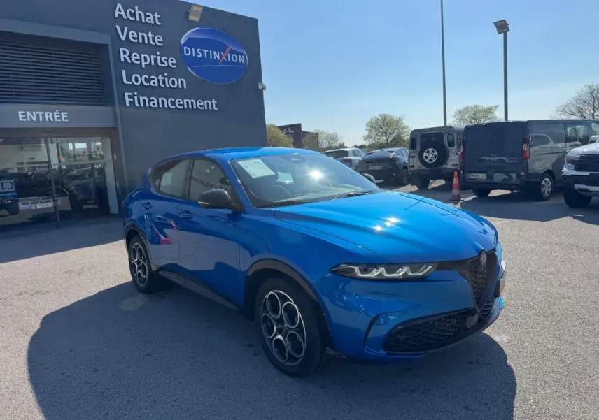 Vue 3/4 avant droite d'une Alfa Romeo Tonale bleu foncé avec jantes alliage 18 pouces, stationnée devant un concessionnaire.
