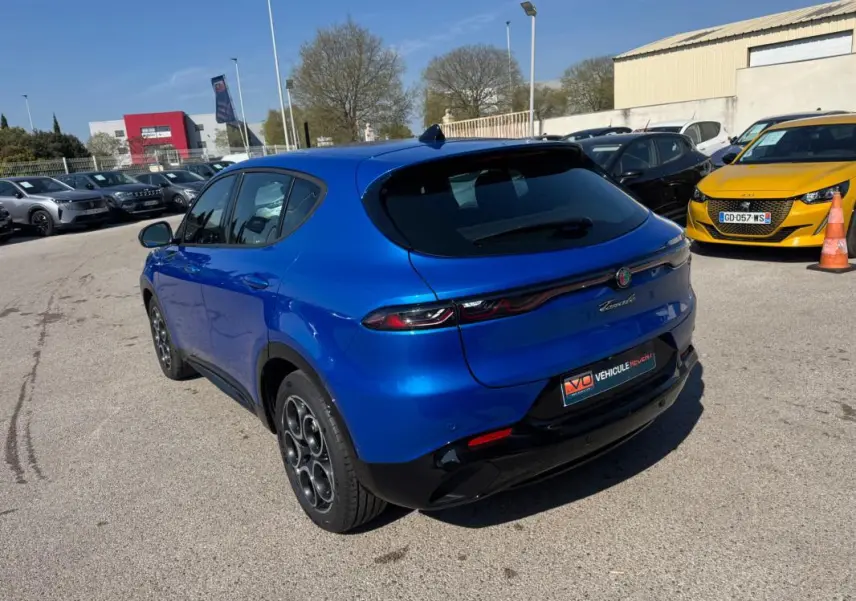 Vue 3/4 arrière gauche de l'Alfa Romeo Tonale bleu foncé avec jantes alliage 18 pouces sur parking extérieur.