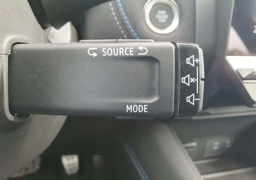 Gros plan sur la commande au volant du Renault Captur 2026, avec bouton source et mode, intérieur noir et surpiqûres bleues.