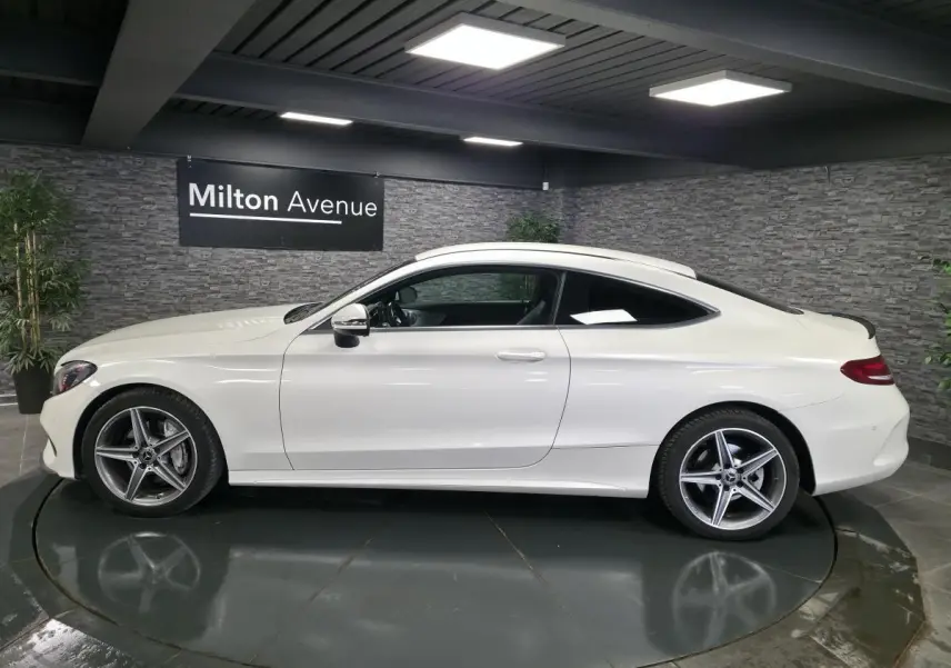 Vue latérale droite d'une Mercedes Classe C Coupé blanc nacré avec jantes alliage AMG à 5 branches dans un showroom.