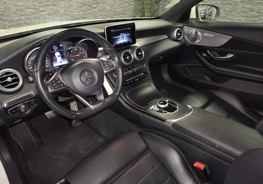 Vue intérieure côté conducteur de la Mercedes Classe C Coupé 2017, avec tableau de bord noir et volant sport AMG.