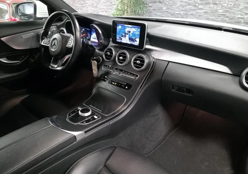 Vue intérieure côté conducteur du tableau de bord noir et console centrale avec écran GPS de la Mercedes Classe C Coupé blanc.