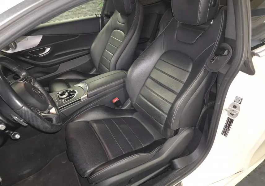 Vue intérieure côté conducteur d'un Mercedes Classe C Coupé blanc, sièges sport en cuir noir avec surpiqûres grises.