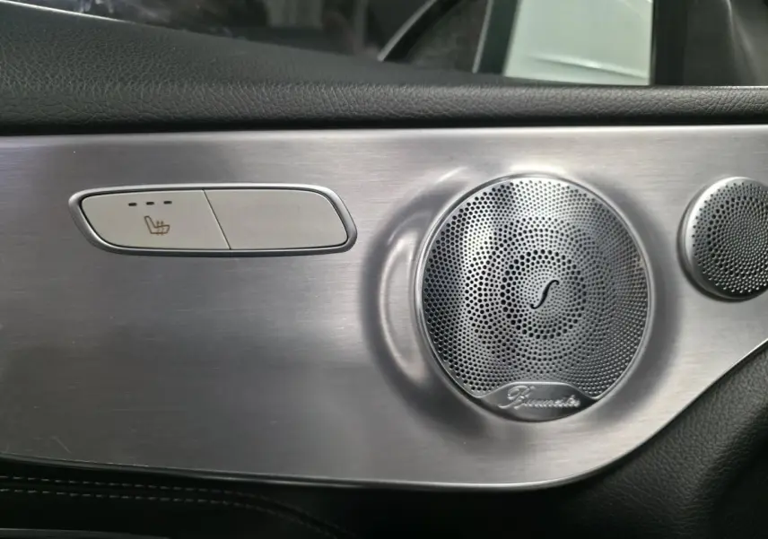 Détail intérieur côté porte avec bouton de siège chauffant et haut-parleur Burmester en finition aluminium brossé.