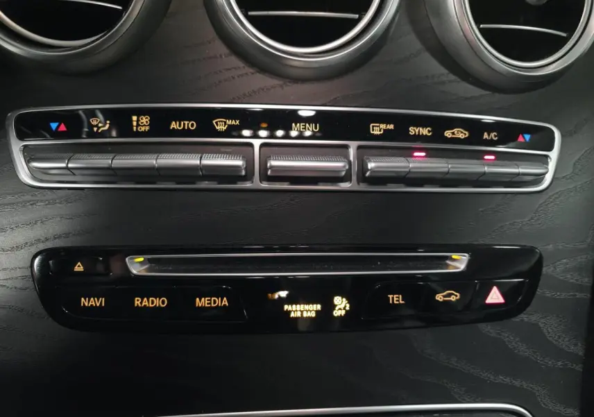 Vue rapprochée de la console centrale noire avec commandes climatisation et multimédia d'une Mercedes Classe C Coupé blanc.