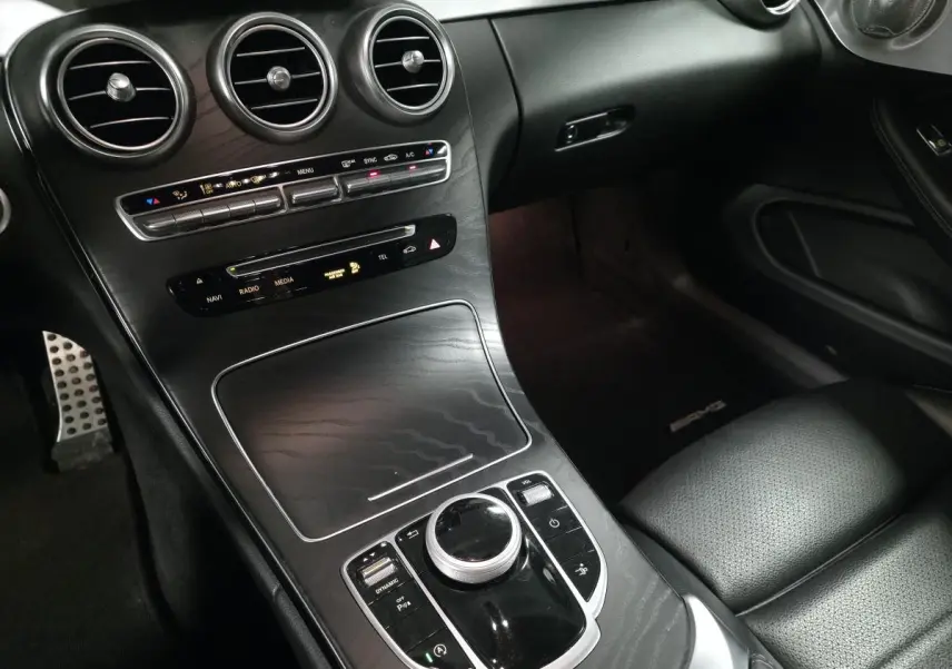 Vue intérieure côté passager du tableau de bord et console centrale noire avec commandes multimédia et aérateurs ronds Mercedes AMG.