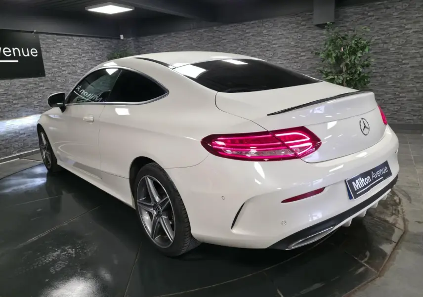 Vue 3/4 arrière droite d'une Mercedes Classe C Coupé blanc avec jantes AMG 5 branches et feux arrière LED allumés.