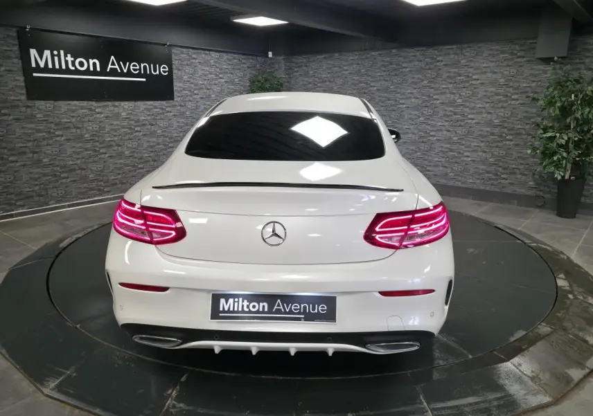 Vue arrière d'un Mercedes Classe C Coupé blanc avec feux LED allumés et double sortie d'échappement chromée.