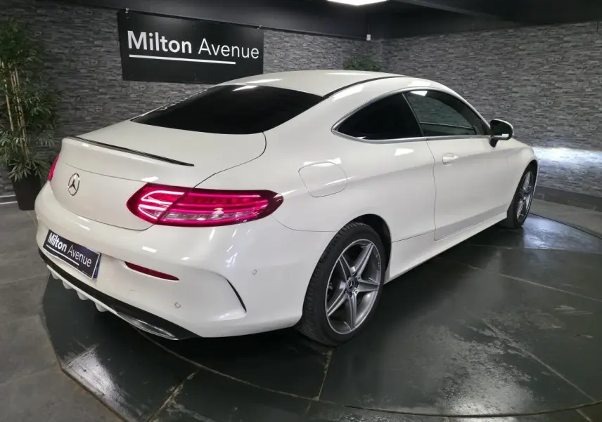 Mercedes Classe C Coupé blanc vue 3/4 arrière droit, jantes AMG 5 branches et feux arrière LED allumés.