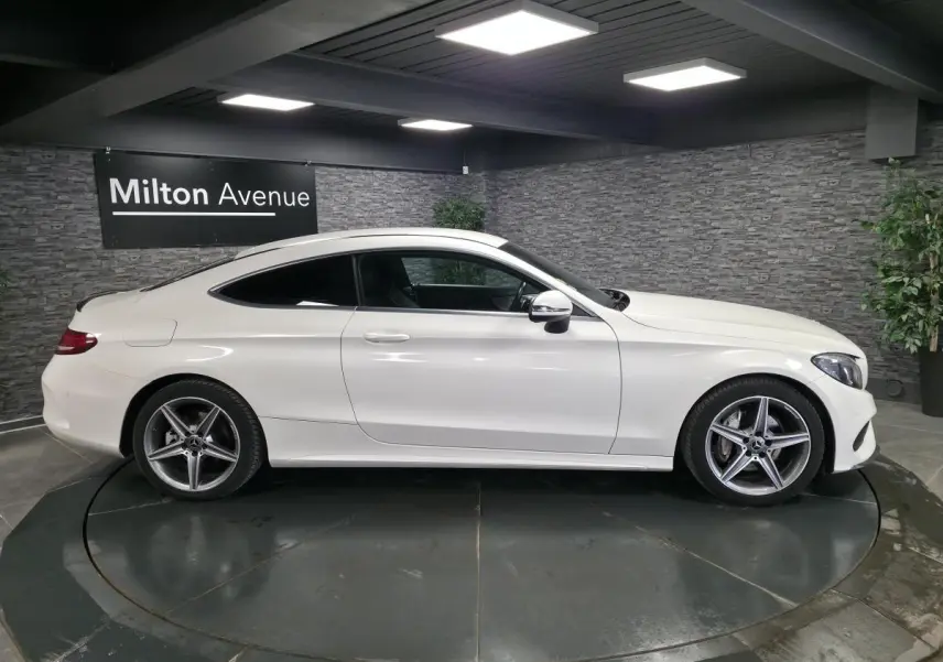 Vue latérale droite d'un coupé Mercedes Classe C blanc avec jantes alliage AMG 5 branches dans un showroom.