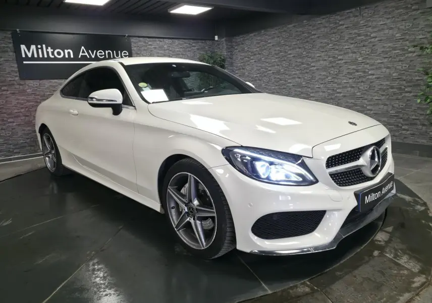 Mercedes Classe C Coupé blanc vu en 3/4 avant droit, avec jantes AMG 5 branches et phares LED allumés.