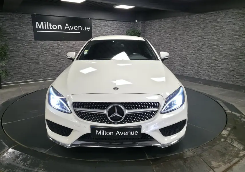 Vue avant d'une Mercedes Classe C Coupé blanc avec calandre AMG et phares LED allumés en showroom.