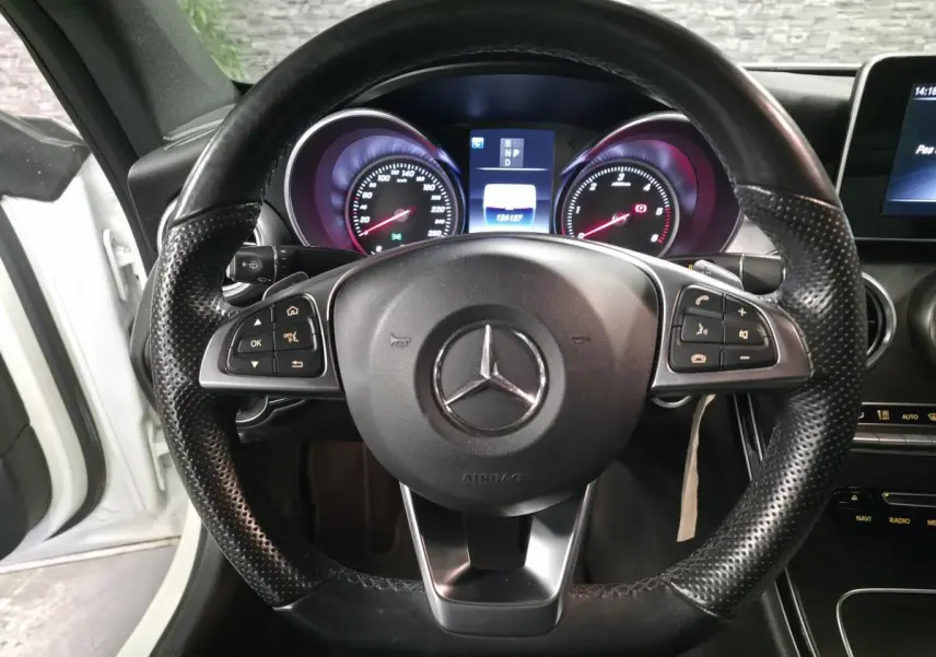 Vue rapprochée du volant sport en cuir noir perforé d’une Mercedes Classe C Coupé blanc, avec tableau de bord digital allumé.