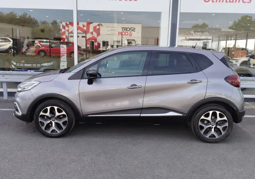 Renault Captur Gris Cassiopée vu de profil côté gauche, avec jantes bi-ton et vitres teintées.