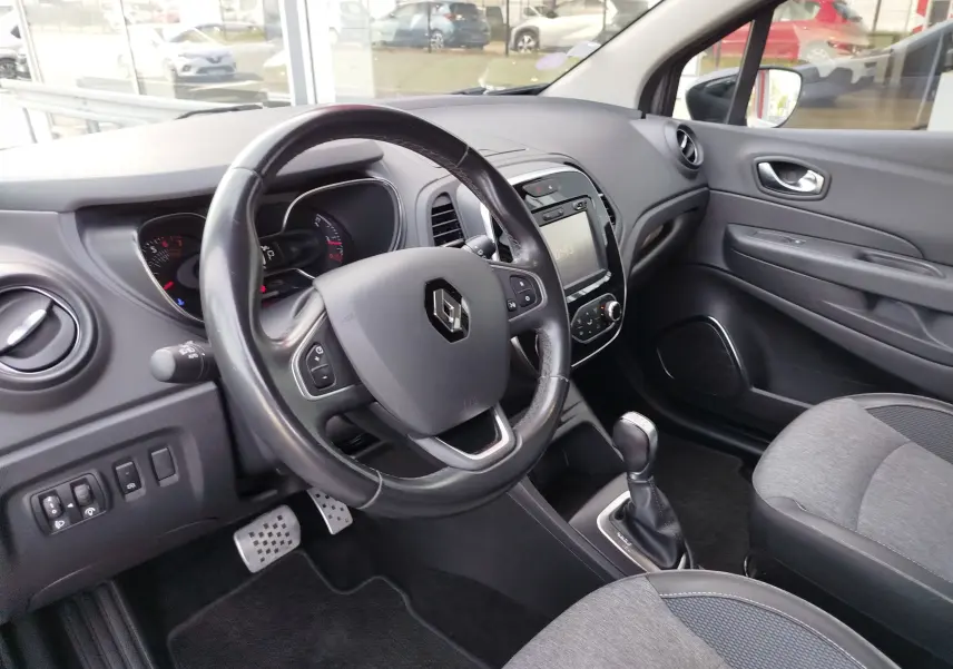 Vue intérieure côté conducteur du Renault Captur gris, avec volant multifonction, écran tactile et levier de boîte automatique.