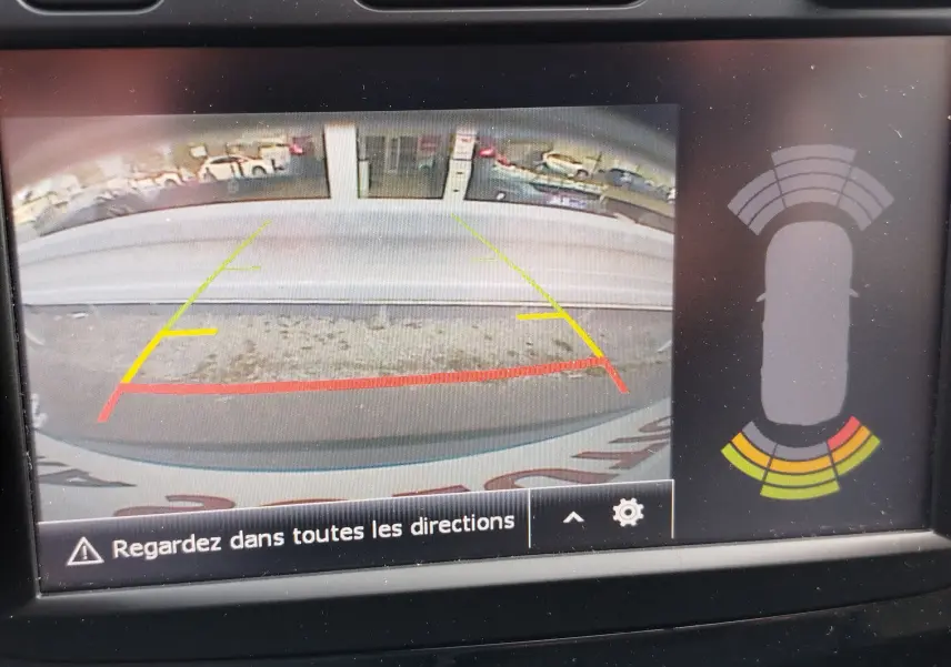 Vue de la caméra de recul du Renault Captur gris Cassiopée, avec lignes de guidage colorées et capteurs d'obstacles affichés.