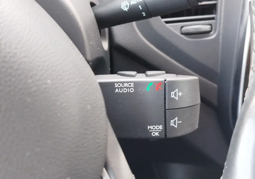 Gros plan sur les commandes audio au volant du Renault Captur gris Cassiopée, avec boutons de volume et gestion d'appels.