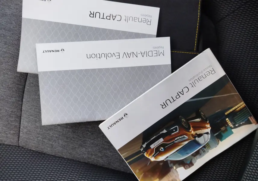 Brochures Renault Captur posées sur un siège, couverture montrant un Captur orange en 3/4 avant dans un décor urbain.