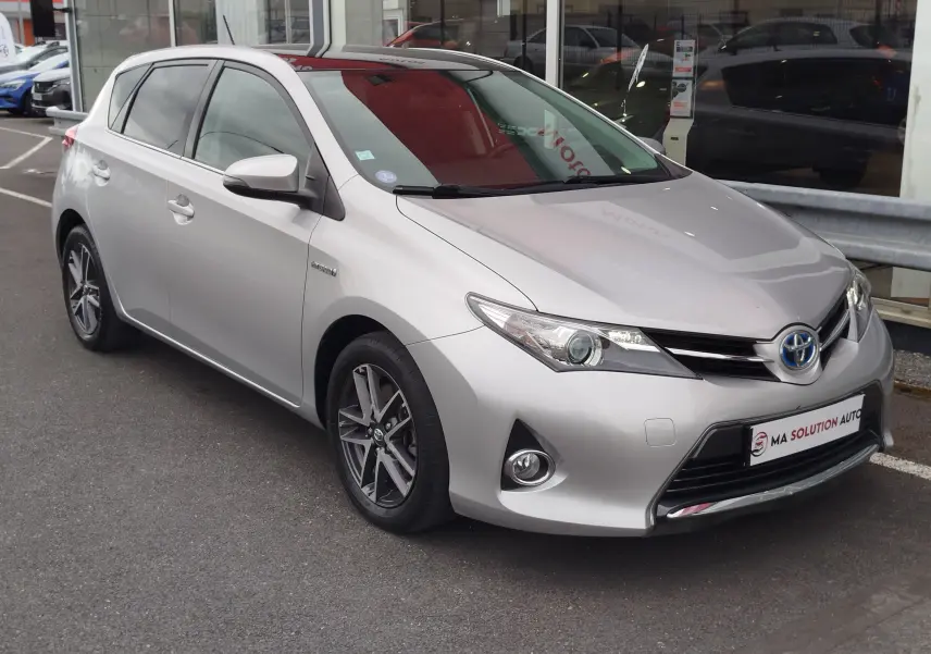 Toyota Auris HSD 136h gris aluminium vue 3/4 avant droit, avec jantes alliage et calandre distinctive hybride.