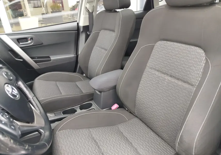 Vue intérieure côté conducteur de la Toyota Auris HSD 136h 2015, sièges tissu gris avec surpiqûres blanches.