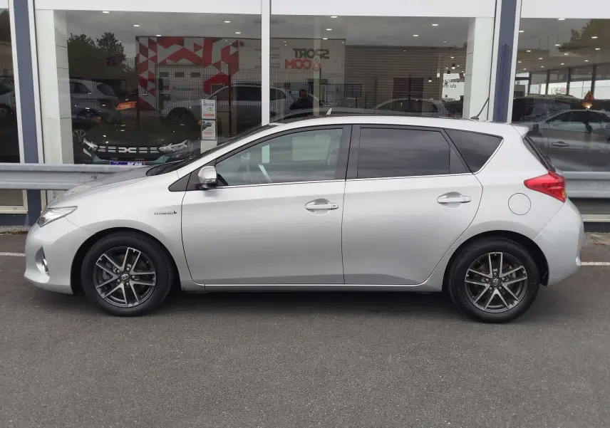 Profil droit d'une Toyota Auris HSD 136h gris aluminium de 2015, avec jantes alliage et vitres teintées.