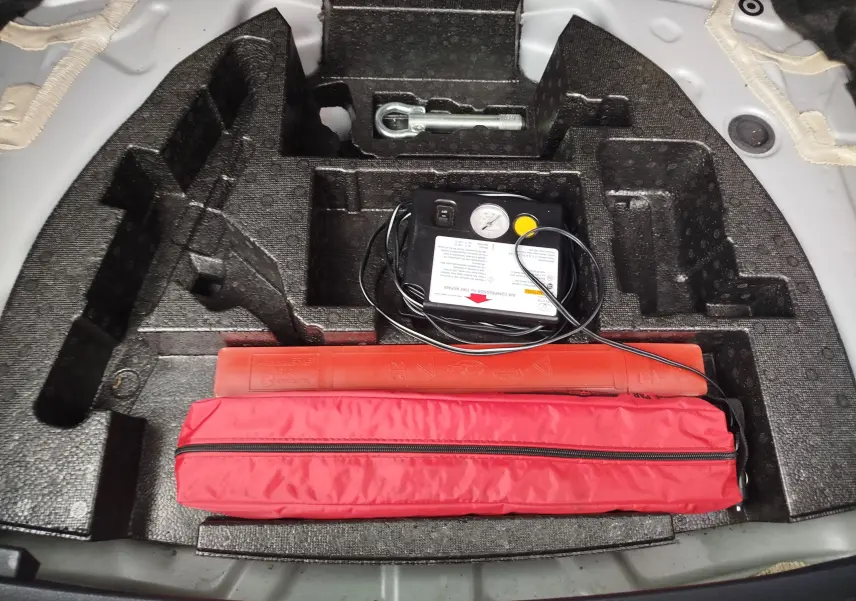 Vue plongeante sur le rangement de coffre d’une Toyota Auris gris aluminium, avec kit de réparation pneus et triangle de signalisation rouge.