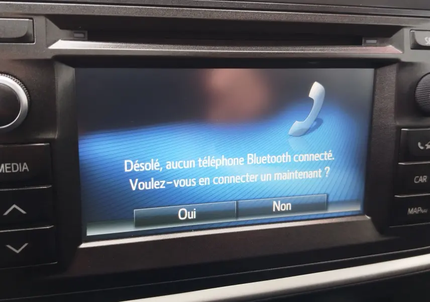 Écran central de la Toyota Auris HSD 136h 2015 affichant un message Bluetooth, entouré de commandes noires.