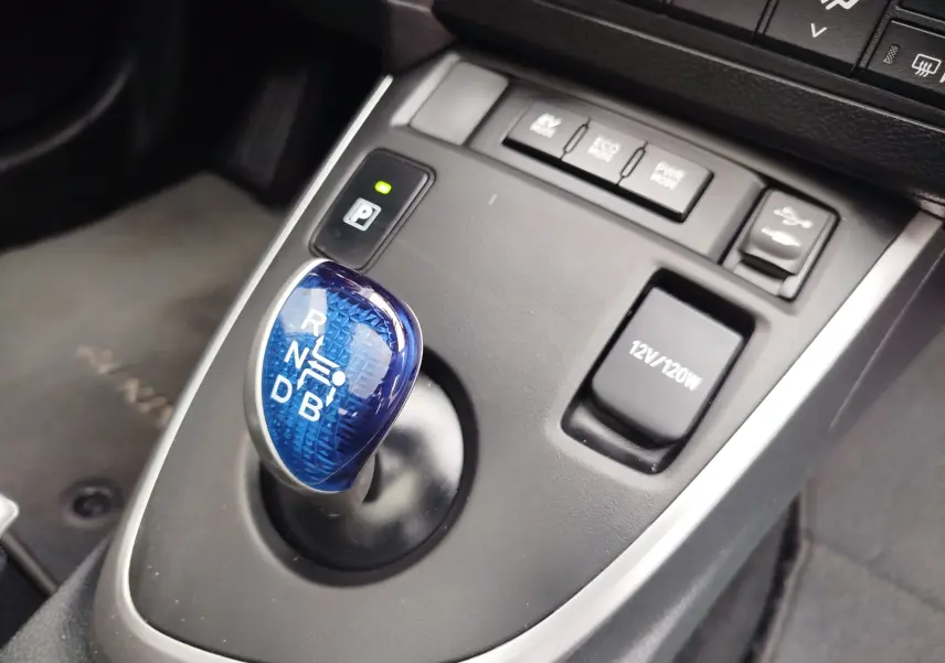 Gros plan sur le levier de vitesses bleu de la Toyota Auris HSD 136h 2015, entouré des boutons de modes de conduite et prise 12V.