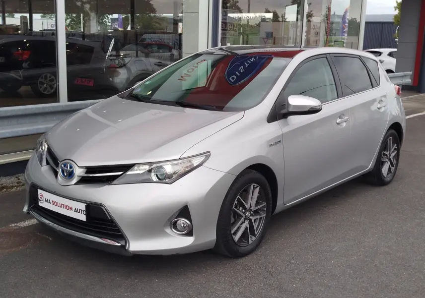 Toyota Auris HSD 136h gris aluminium vue 3/4 avant droit, avec jantes alliage et badge hybride sur aile avant.