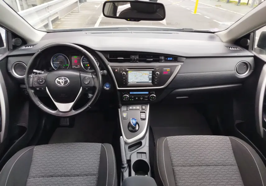 Vue intérieure frontale du tableau de bord et volant noir de la Toyota Auris hybride 2015 avec écran GPS et commandes au volant.